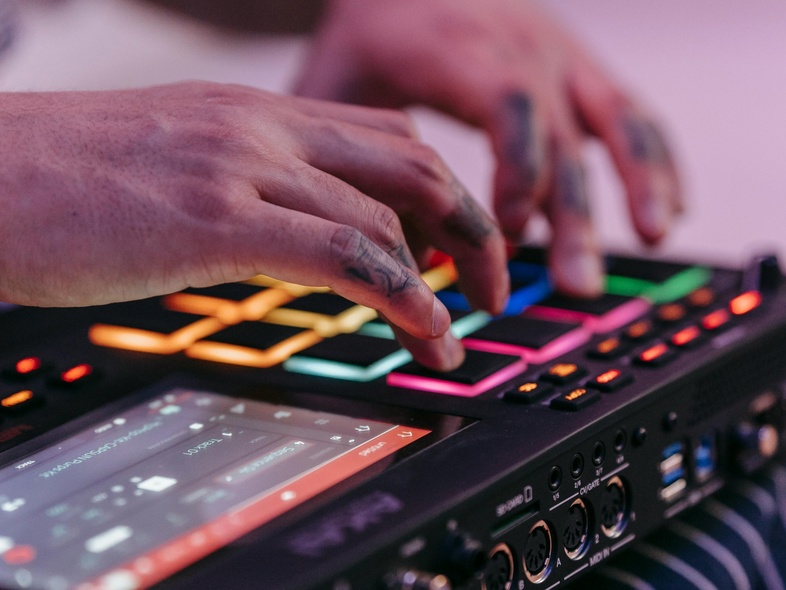 Närbild på händer som spelar på en färgglad musikproduktionsmaskin med knappar och skärm.