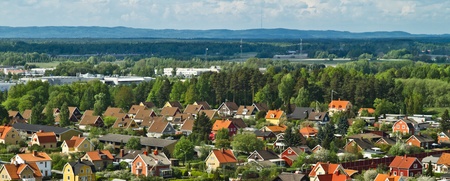 Färgglada villor med röda och gula tak i ett lummigt bostadsområde, omgivna av skog och berg i bakgrunden.