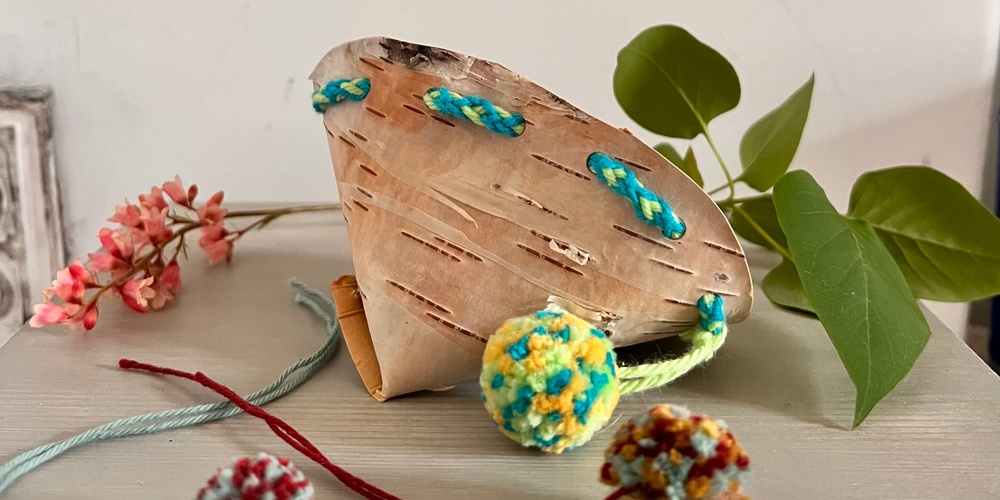 En dekorerad bit björkbark med färgglada garnbollar och gröna blad på ett bord.