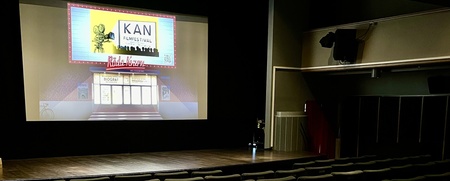 En tom biosalong med rader av stolar och en filmduk som visar en affisch för en filmfestival.