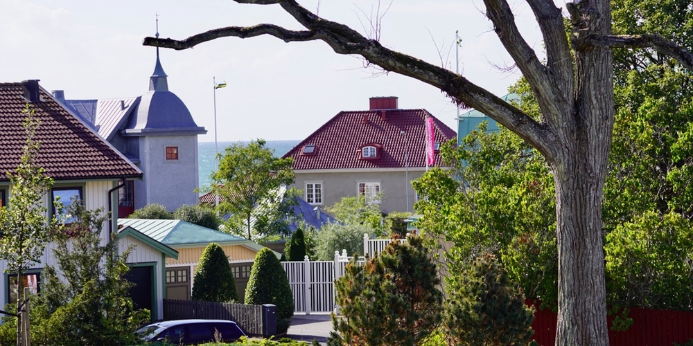Vy över ett bostadsområde med färgglada hus, trädgårdar och ett stort träd i förgrunden.