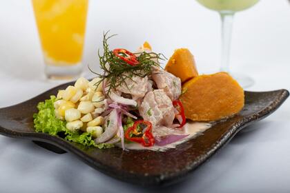 En tallrik med ceviche, sötpotatis, majs och sallad, serverad med drycker i bakgrunden.