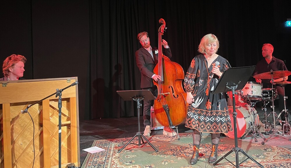 Fyra musiker uppträder på scen, med piano, kontrabas, trummor och sångerska vid mikrofon.