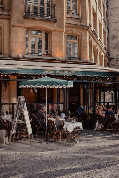 Uteservering vid ett parisiskt café med gäster som sitter vid bord under en grön markis.