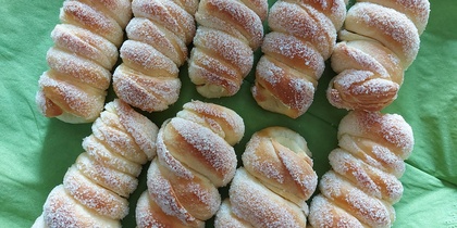 Nio sockerströdda, spiralformade bröd ligger på en grön duk.