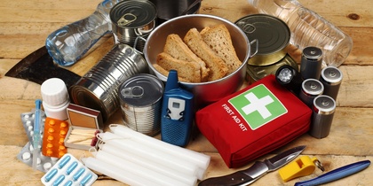 Nödutrustning med konserver, vattenflaskor, första hjälpen-kit, ficklampa, kniv, ljus och mediciner på ett träbord.