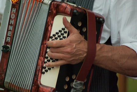 En person spelar på ett rödbrunt dragspel av märket Hohner, fokus på handen och instrumentet.