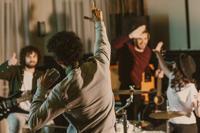 Ett band repeterar i en studio, sångaren sjunger i mikrofon och bandmedlemmar spelar instrument och hejar på varandra.