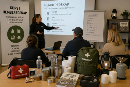 Personer deltar i en kurs om hemberedskap med nödutrustning på bordet, presentation och checklista synliga.