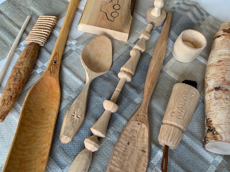 Handgjorda träföremål, som skedar och koppar, ligger på en gråmönstrad duk.