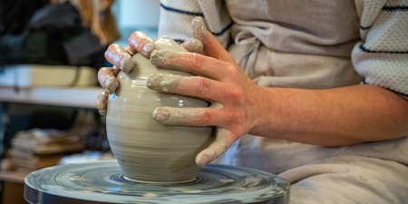 En person formar lera på en drejskiva i en keramikverkstad.