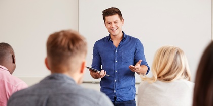 En man står framför en grupp och håller en presentation i ett klassrum.