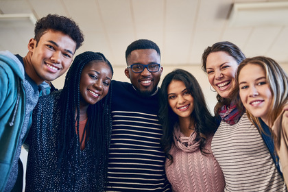 Sex unga vuxna står tätt tillsammans och ler mot kameran i ett ljust rum.