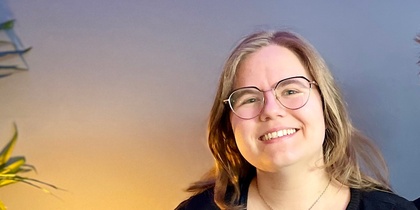 Två leende personer sitter tillsammans i en blå soffa i ett rum med blå vägg och grön växt.