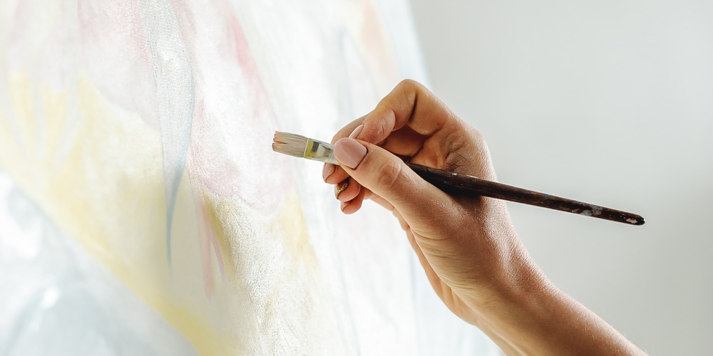 En hand målar på en duk med en pensel, palett med färg syns i förgrunden.