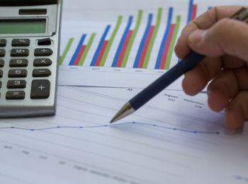 En hand håller en penna över ett papper med diagram och en miniräknare bredvid.