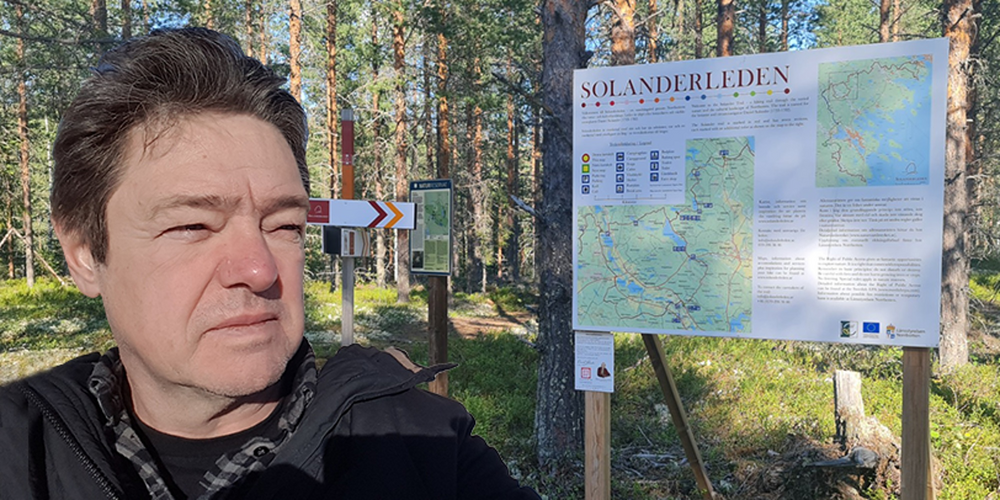 Person tar selfie vid en informationsskylt om Solanderleden i en solig skogsmiljö.