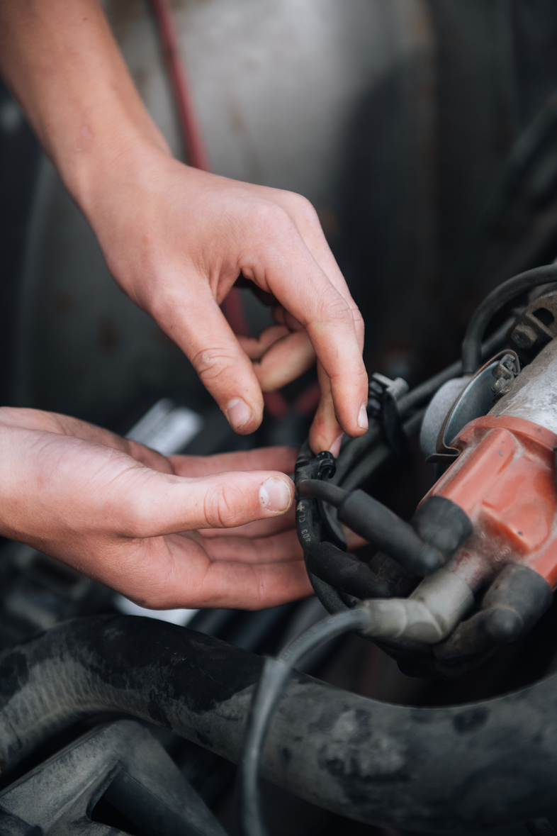 Närbild på händer som arbetar med kablar i en bilmotor.