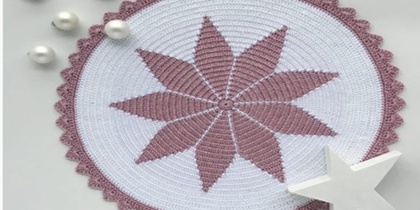 Rund virkad duk med stjärnmönster i lila och vitt, dekorerad med pärlor och en vit stjärnformad prydnad.