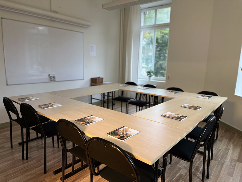 Ett tomt mötesrum med U-formade bord, svarta stolar och anteckningsblock vid varje plats.