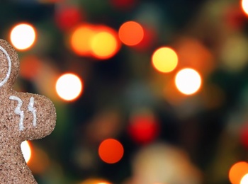 En pepparkaksgubbe hänger i ett snöre framför en suddig bakgrund med färgglada julbelysningar.