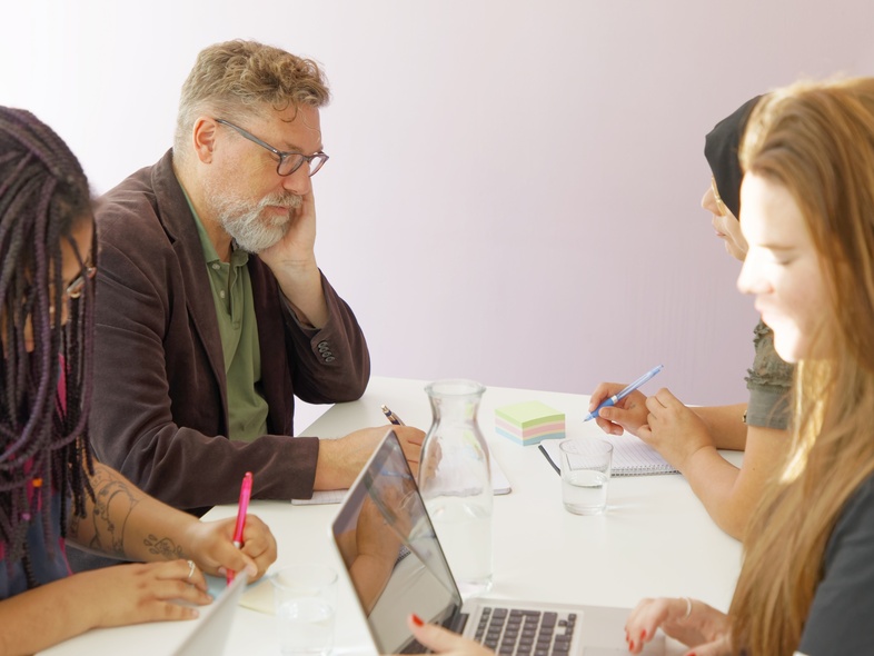 Fyra personer sitter runt ett bord och arbetar tillsammans med datorer och anteckningar.