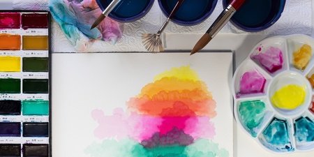 Ett akvarellmålningsset med färger, penslar och en målning i regnbågens färger på ett vitt papper.