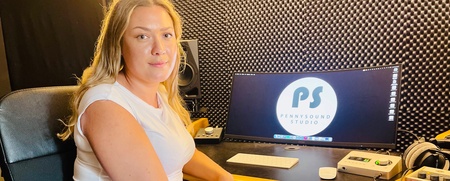 Kvinna i vit klädsel sitter i en musikstudio framför en datorskärm med logotypen 'PS'.