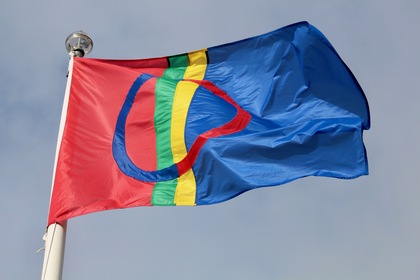 Samiska flaggan vajar mot en blå himmel. Flaggan har rött, blått, grönt och gult med en cirkel i mitten.