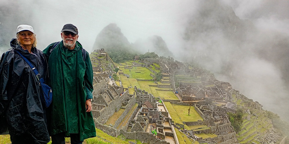 Två personer i regnkläder står framför Machu Picchu i dimma och regn.