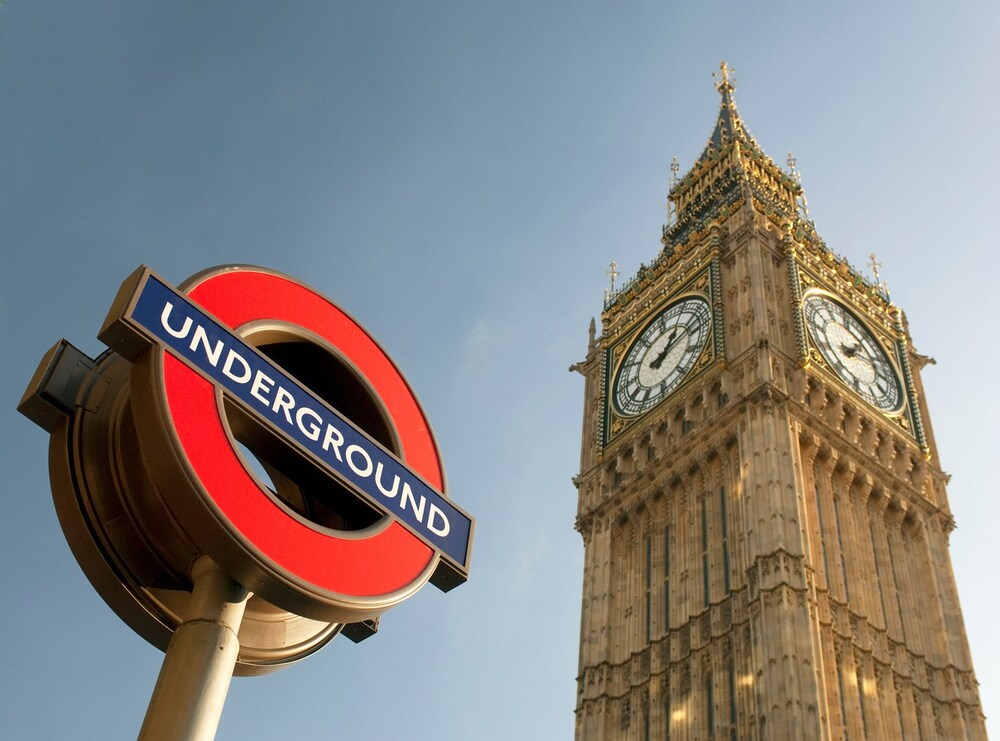 London Underground-skylt framför Big Ben under en klar himmel.
