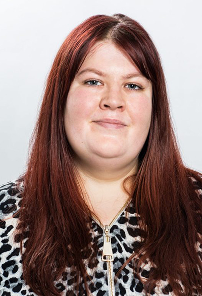 Person med långt rödbrunt hår och leopardmönstrad tröja mot ljus bakgrund.