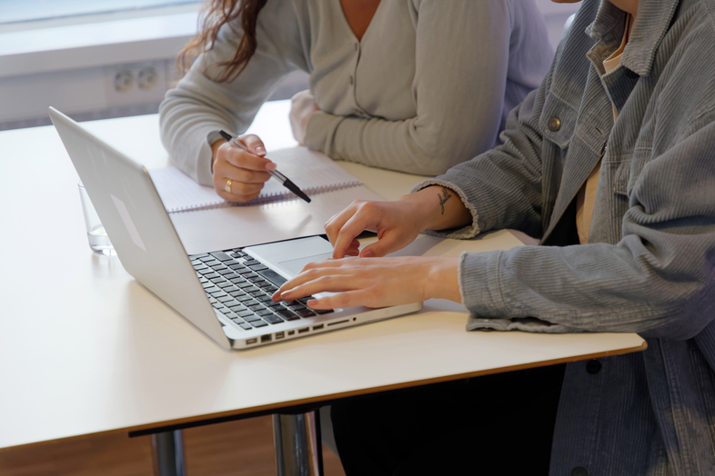 Två personer sitter vid ett bord, en skriver på en laptop och den andra antecknar i ett block.