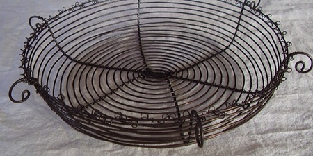 En rund korg av svart metalltråd med spiralformad botten och dekorativa öglor längs kanten.