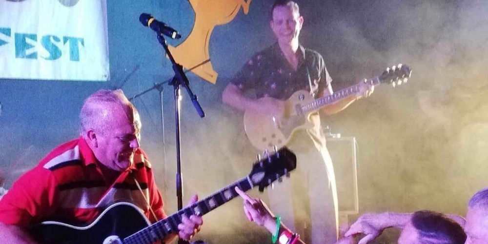 Livlig konsert med gitarrister på scen och entusiastisk publik nära scenen.