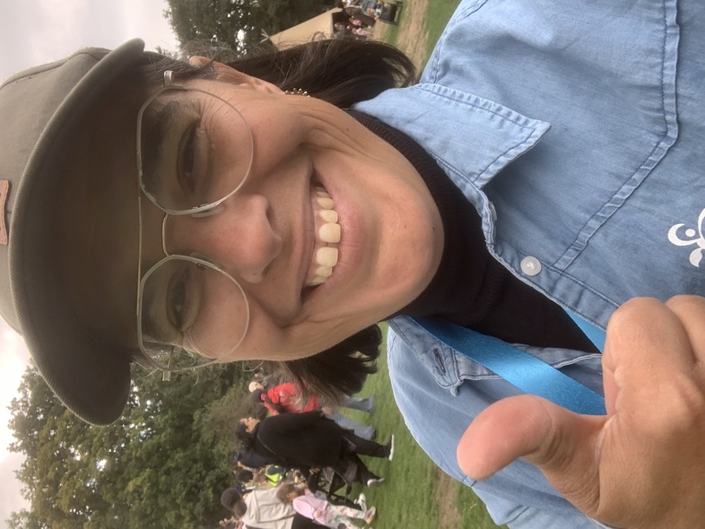 Person med keps och blå skjorta ger tummen upp på en utomhustillställning med folk i bakgrunden.