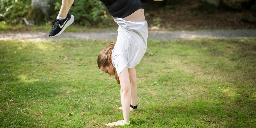 En person gör en handvolt på gräset i en grönskande park.