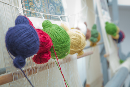 Flera garnnystan i olika färger hänger på en vävstol, redo att användas för vävning.