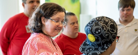 En grupp personer, några med Downs syndrom, står tillsammans inomhus och samtalar.