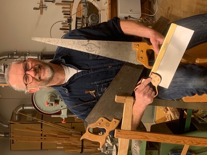 Person i snickarverkstad håller tre olika typer av sågar i händerna, omgiven av trä och verktyg.