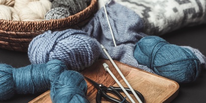 Garnnystan, stickor och sax ligger på en bricka och i en korg, redo för stickning.