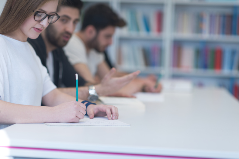 Studenter sitter vid ett bord och skriver i ett klassrum eller bibliotek.