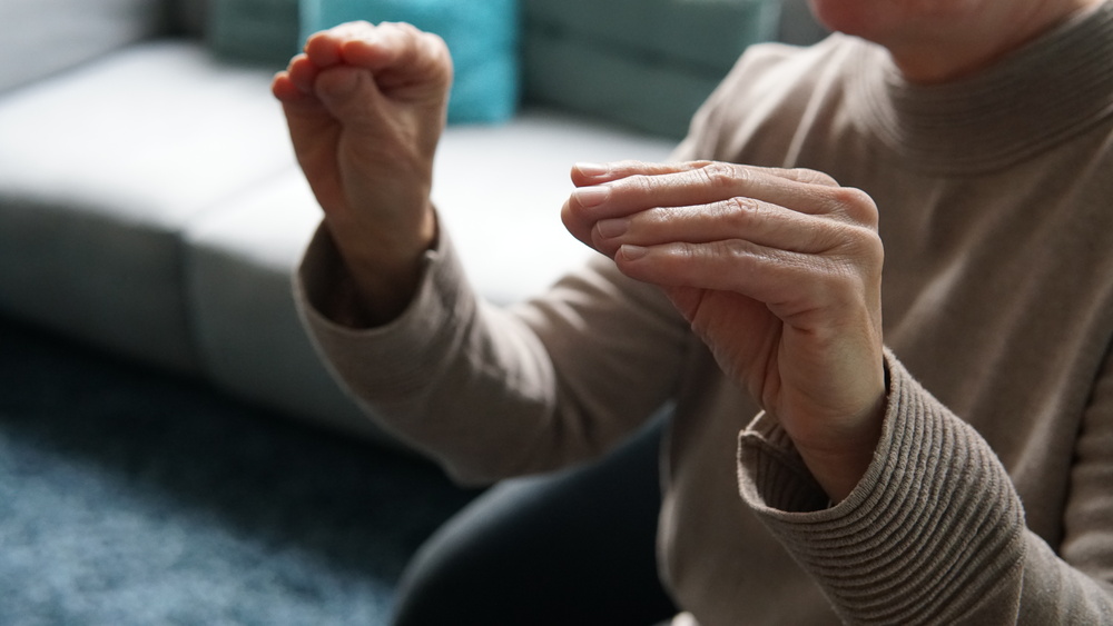 En person visar teckenspråk med händerna i fokus, sittande i en soffa inomhus.
