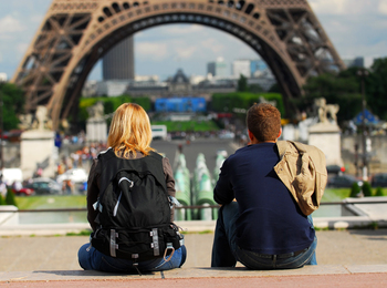 Två personer sitter med ryggen mot kameran och tittar mot Eiffeltornet i Paris.