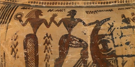 Två stiliserade figurer i svart på en antik grekisk vas, med geometriska mönster runtom.