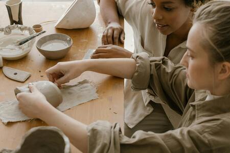 Två personer arbetar med keramik vid ett träbord, formar lera med händerna.