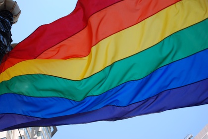 En regnbågsflagga vajar mot en blå himmel, symbol för HBTQ+-rörelsen.