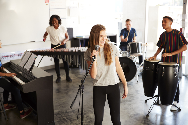 En grupp ungdomar spelar olika instrument och sjunger tillsammans i ett ljust klassrum.