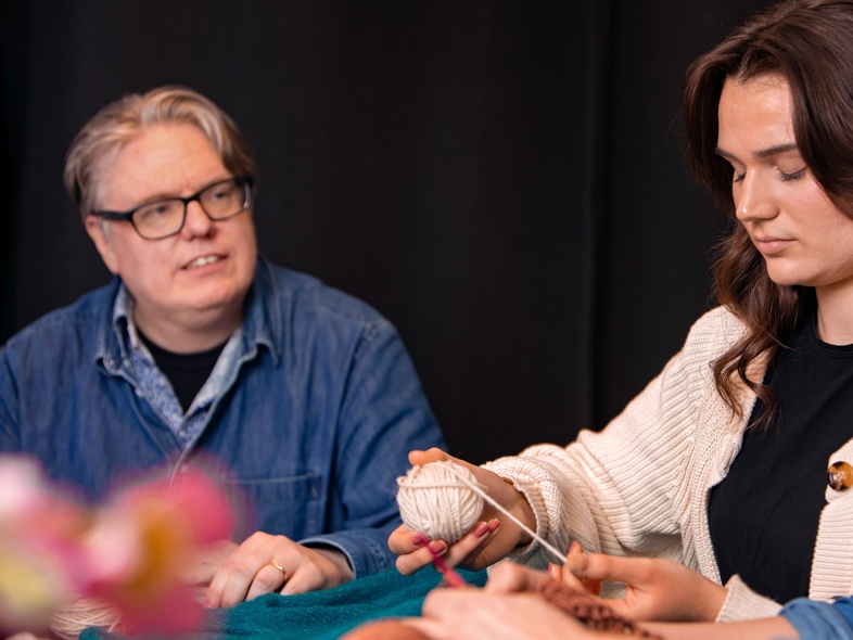 Tre personer sitter tillsammans och stickar, två kvinnor och en man, i en avslappnad miljö.