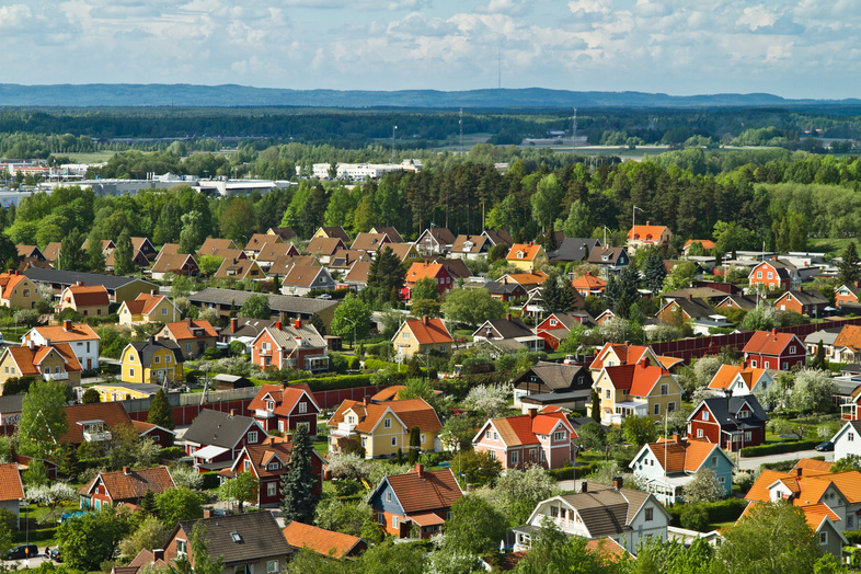 Färgglada villor med röda och gula tak i ett lummigt bostadsområde, omgivna av skog och berg i bakgrunden.